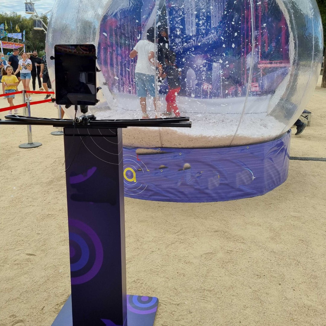 ipad on a rail on top of a branded column in front of a large snow globe with people in it